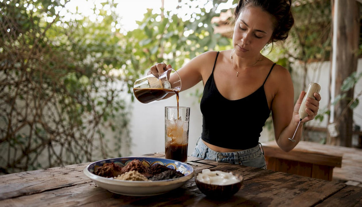 Woman pouring iced coffee over ice at home